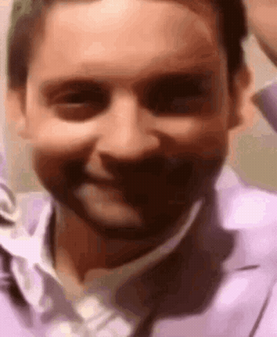 A Close Up Of A Man 'S Face In A Purple Shirt And Tie Smiling . GIF