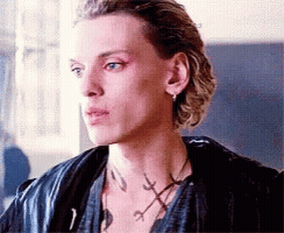 A Close Up Of A Man 'S Face Wearing A Leather Jacket And A Necklace . GIF