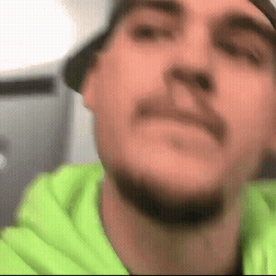 A Close Up Of A Man 'S Face With A Beard Wearing A Green Hoodie GIF