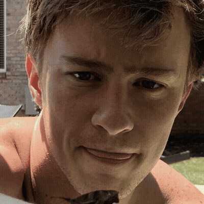 A Close Up Of A Man 'S Face With A Brick Building In The Background GIF