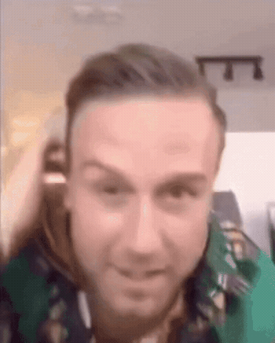 A Close Up Of A Man 'S Face With A Green Shirt On And A Blurred Background . GIF