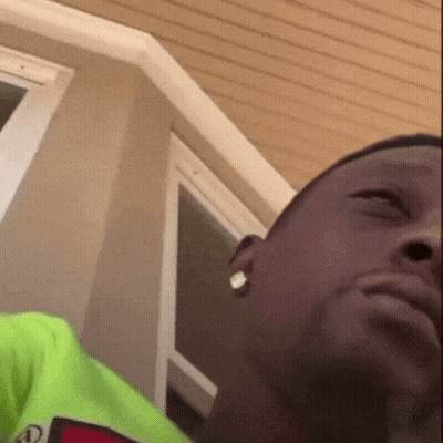 A Close Up Of A Man 'S Face With A Green Shirt On And Earrings . GIF