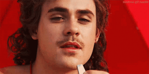 A Close Up Of A Man 'S Face With A Mustache Holding A Piece Of Paper In His Hand . GIF