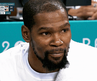 A Close Up Of A Man 'S Face With A Scoreboard Behind Him That Says Olympic Games In Blue GIF