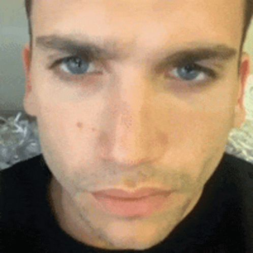 A Close Up Of A Man 'S Face With Blue Eyes And A Black Shirt On GIF