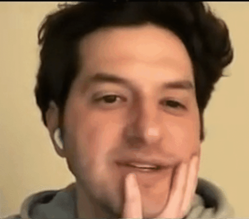 A Close Up Of A Man 'S Face With His Hand On His Chin And Headphones On . GIF