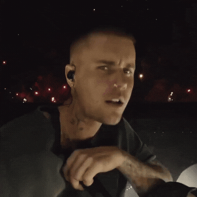 A Close Up Of A Man Singing Into A Microphone With Fireworks In The Background GIF