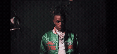 A Close Up Of A Man Wearing A Green Jacket And A Necklace . GIF