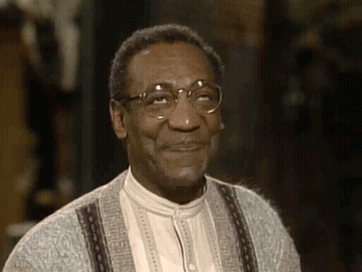A Close Up Of A Man Wearing Glasses And A Sweater Smiling GIF