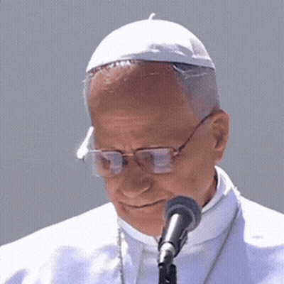 A Close Up Of A Man Wearing Glasses And A White Hat Speaking Into A Microphone GIF