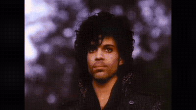 A Close Up Of A Man With Curly Hair Wearing A Black Coat And Looking At The Camera . GIF