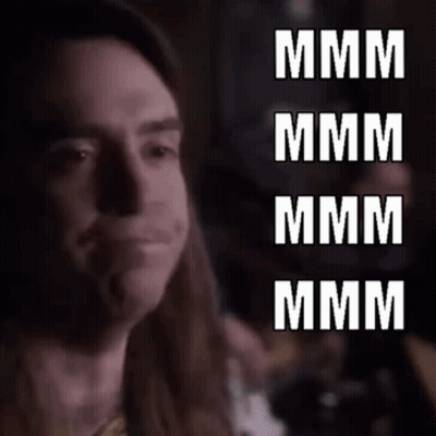 A Close Up Of A Man With Long Hair Making A Funny Face With The Words `` Mmmm '' Written In White Letters . GIF
