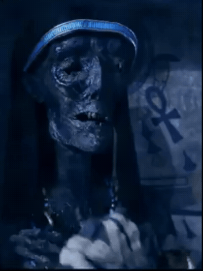 A Close Up Of A Mummy With An Ankh Symbol On The Wall Behind Him GIF