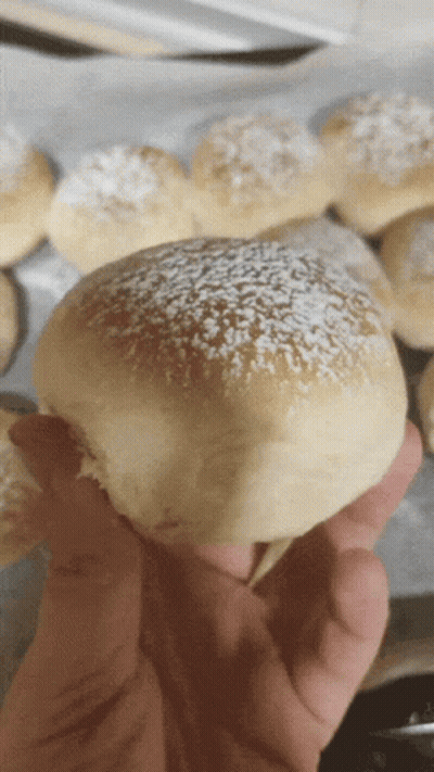 A Close Up Of A Person Holding A Bun With Powdered Sugar On Top GIF