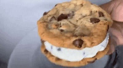A Close Up Of A Person Holding A Chocolate Chip Cookie Sandwich With Ice Cream . GIF