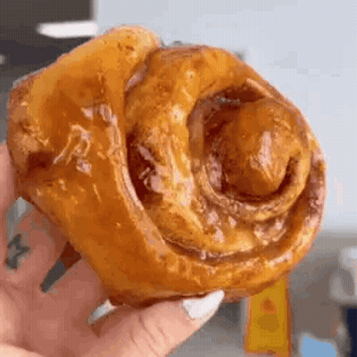 A Close Up Of A Person Holding A Cinnamon Roll . GIF