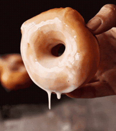A Close Up Of A Person Holding A Glazed Doughnut GIF