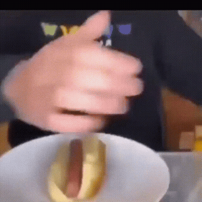 A Close Up Of A Person Holding A Hot Dog With Mustard On It GIF