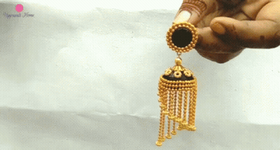 A Close Up Of A Person Holding A Pair Of Gold Earrings With A Black Circle In The Middle GIF