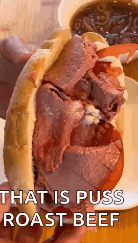 A Close Up Of A Person Holding A Roast Beef Sandwich With A Cup Of Soup In The Background . GIF
