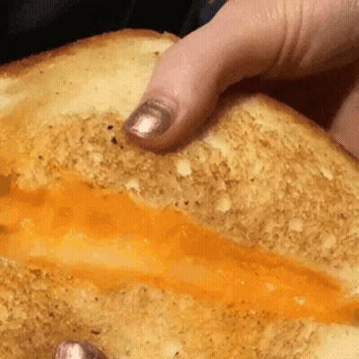 A Close Up Of A Person Holding A Sandwich With Cheese On It GIF