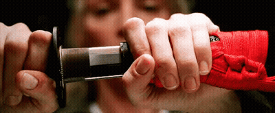 A Close Up Of A Person Holding A Sword With A Red Ribbon Around It GIF