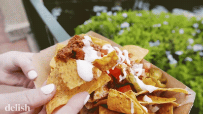 A Close Up Of A Person Holding A Tray Of Nachos With The Word Delish On The Bottom GIF
