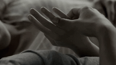 A Close Up Of A Person Laying On A Bed Holding Another Person 'S Hand . GIF