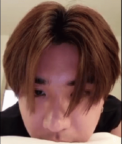 A Close Up Of A Person Laying On A Bed With Their Head On A Pillow And Looking At The Camera . GIF