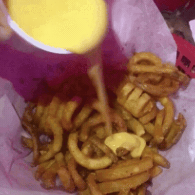 A Close Up Of A Person Pouring Cheese On Curly Fries GIF