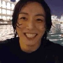 A Close Up Of A Person 'S Face Smiling In Front Of A Body Of Water At Night . GIF
