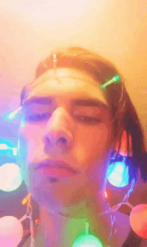 A Close Up Of A Person 'S Face With Christmas Lights Around His Neck GIF