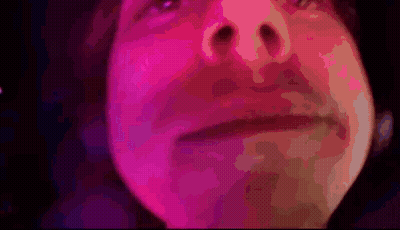A Close Up Of A Person 'S Face With Pink And Purple Lights Behind Them GIF