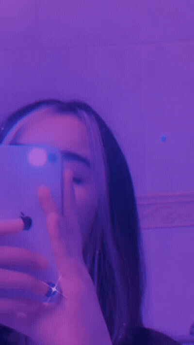 A Close Up Of A Person 'S Face With Purple Lights Behind Her GIF