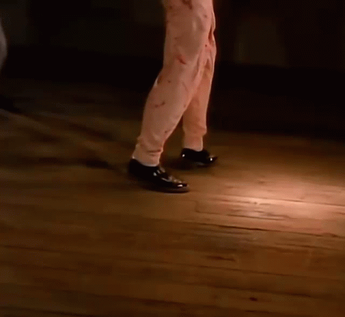 A Close Up Of A Person 'S Feet Wearing Black Shoes Walking On A Wooden Floor . GIF
