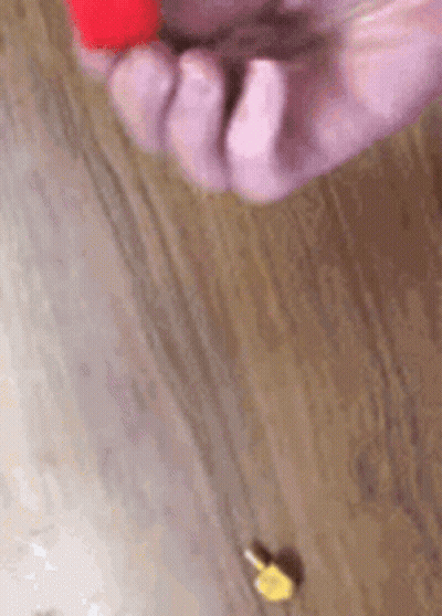 A Close Up Of A Person 'S Hand Holding A Red Object On A Wooden Table . GIF