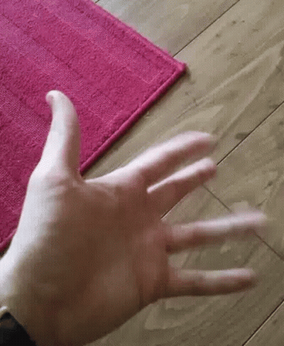 A Close Up Of A Person 'S Hand Reaching Out Towards A Pink Rug On A Wooden Floor . GIF