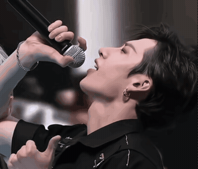 A Close Up Of A Person Singing Into A Microphone With The Letter T On His Shirt GIF