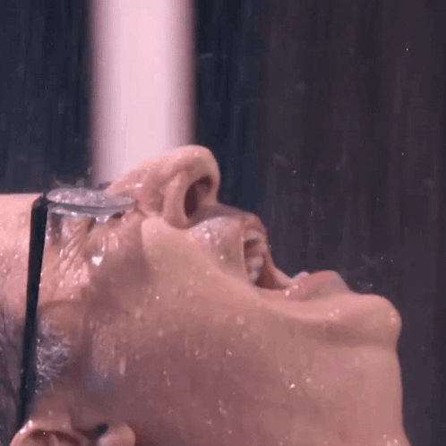 A Close Up Of A Person Taking A Shower With A Glass Of Water In Their Mouth GIF