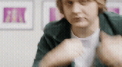 A Close Up Of A Person Wearing A Green Jacket And A White T-Shirt In A Room . GIF