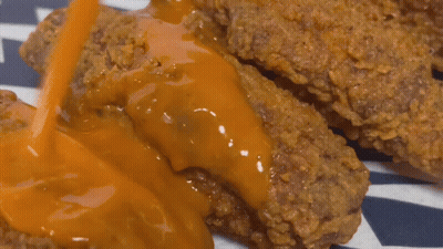 A Close Up Of A Piece Of Fried Chicken Covered In Sauce GIF