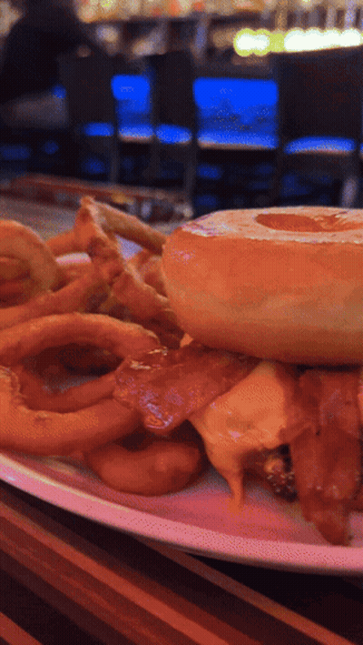 A Close Up Of A Plate Of Food With A Hamburger And Onion Rings GIF