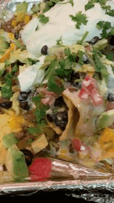 A Close Up Of A Plate Of Nachos With Avocado And Sour Cream On Aluminum Foil GIF
