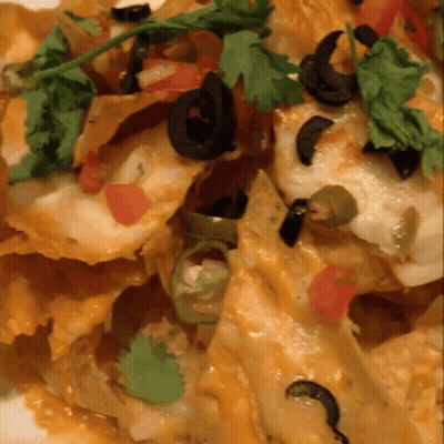 A Close Up Of A Plate Of Nachos With Black Olives And Tomatoes GIF