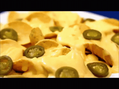 A Close Up Of A Plate Of Nachos With Jalapenos And Cheese GIF