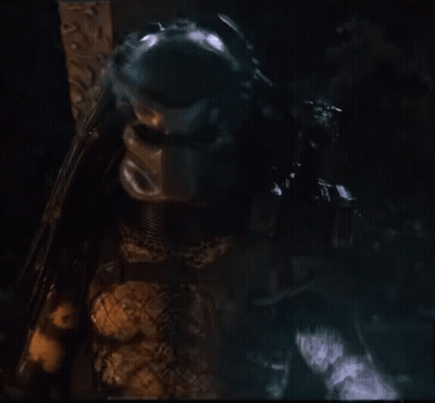 A Close Up Of A Predator Holding A Gun In A Dark Room GIF