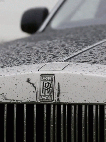 A Close Up Of A Rolls Royce Car With Rain Drops On It GIF