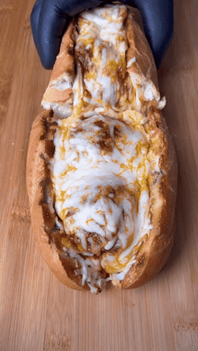 A Close Up Of A Sandwich With Cheese And Sauce On A Wooden Surface GIF