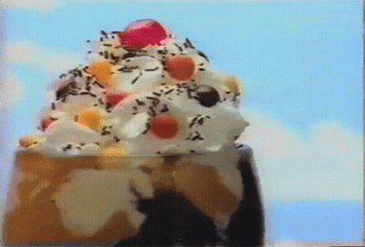 A Close Up Of A Sundae With Whipped Cream , Sprinkles , And A Cherry On Top . GIF