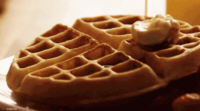 A Close Up Of A Waffle With Syrup And Whipped Cream On It GIF